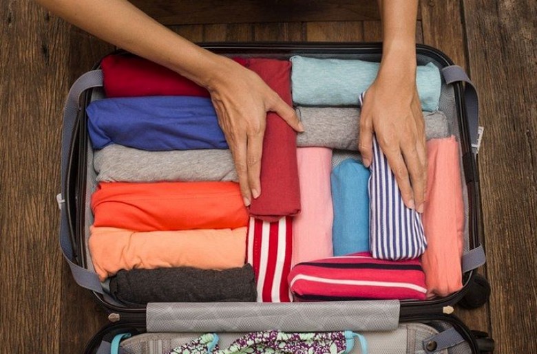 Một vali mở với quần áo nhiều lớp, áo khoác nhẹ, mũ và kính râm xếp gọn gàng